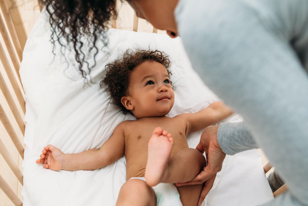 Baby boy lying down with his mother leaning into the crib