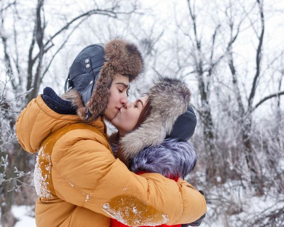 Cute teenage couple holding each other and kissing in wintery forest