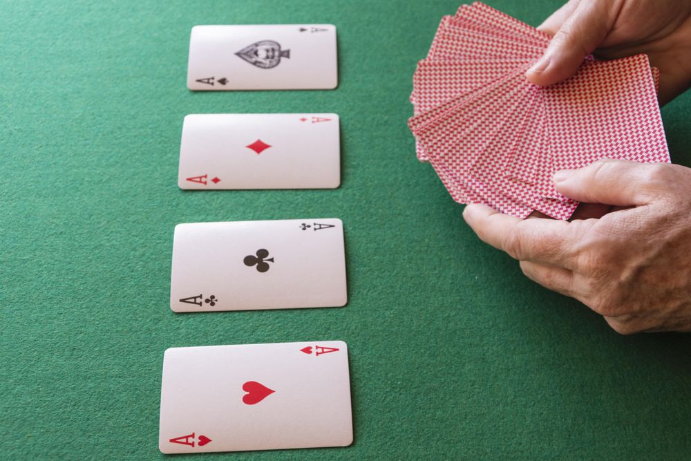 Four aces on table with hands holding playing cards