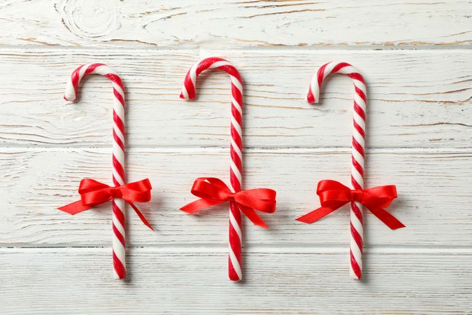 Sweet candy canes with bows on wooden background, space for text