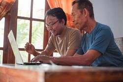 Happy adult son teaching mature father using laptop