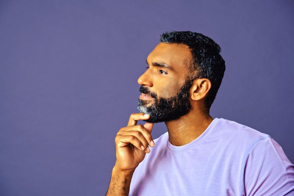 Side view of thoughtful male in purple t-shirt looking at copy space