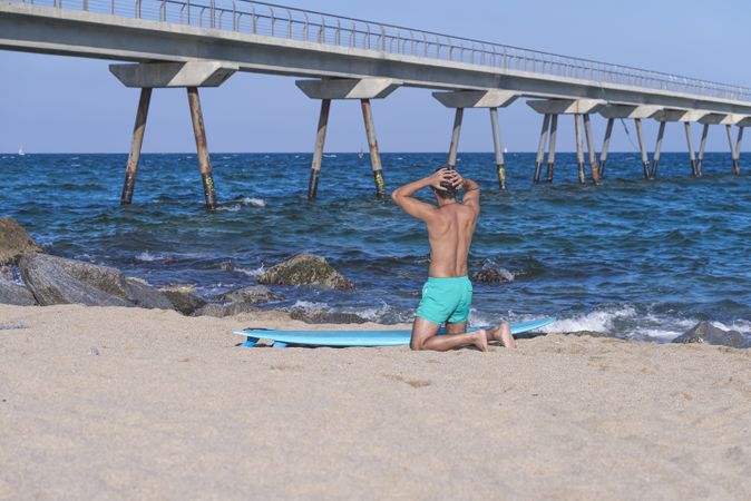 Male surfer kneeling down with surfboard near sea