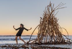Young woman dancing on shore near water and wooden twigs placed for campfire