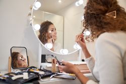 Positive woman applying cosmetic with brush on face looking in m