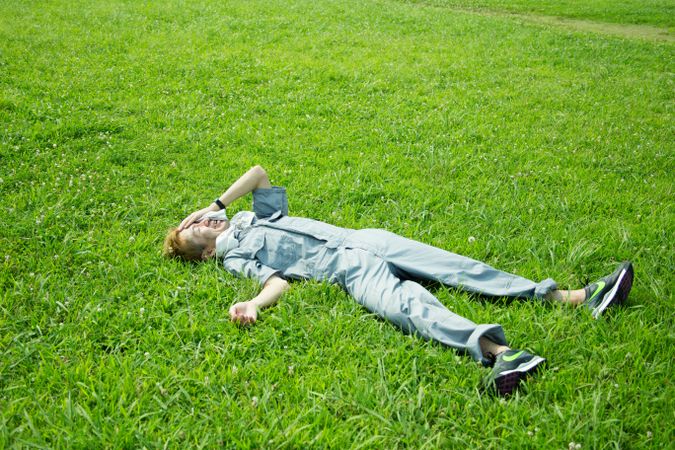 Exhausted man in work suit lying on green grass