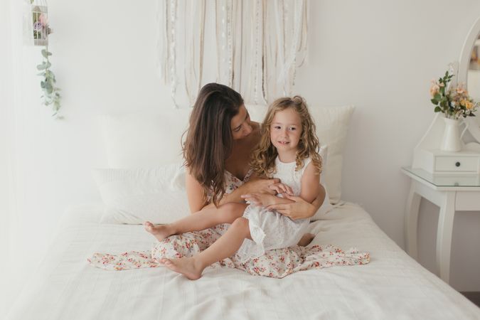 Mother ticking little daughter and laughing on bed