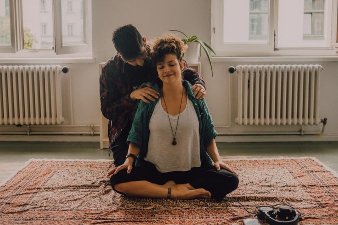Man rubbing shoulders of joyful woman resting on floor at home