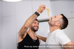 Laughing male couple playfully tasting pasta as they prepare meal 5oXAG4