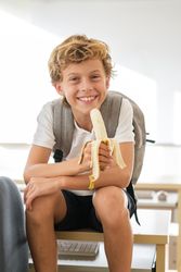 Delighted schoolboy eating banana in classroom