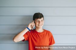 Teenager in red t-shirt standing against wall while using phone 0WOVBr