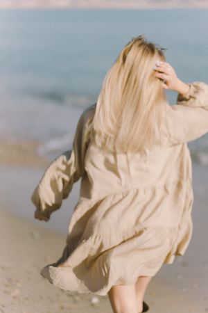 Back view of blonde woman wearing yellow coat walking on seashore