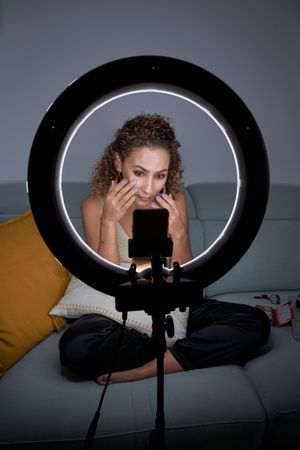 Focused woman recording makeup video on smartphone with ring lam