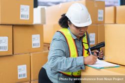 Woman in safety gear working in distribution center checking bar codes on boxes 561qP0