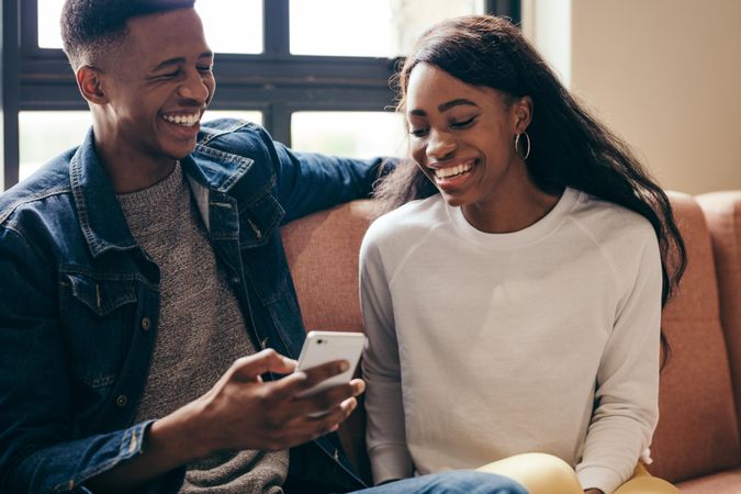 Happy young man and woman sitting on couch with smart phone