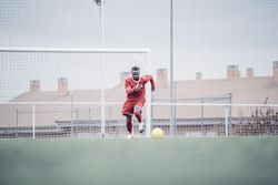 Black soccer player with red outfit playing soccer.