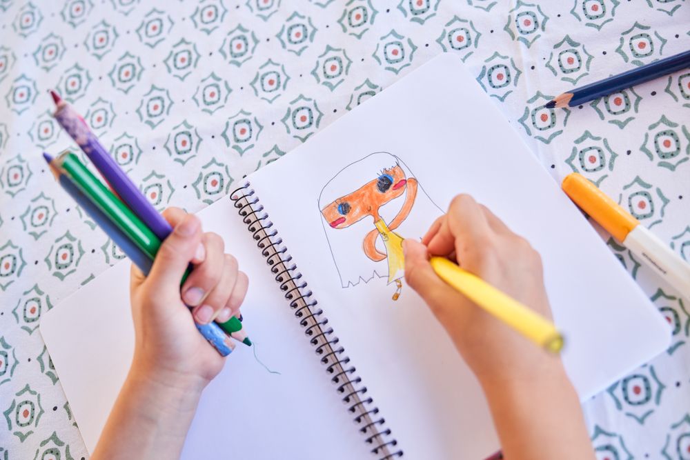 Crop kid drawing picture in notepad at table