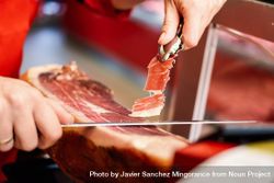 Close up of female hands in butcher shop cutting ham 41XML5
