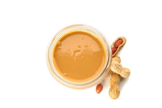 Creamy peanut butter in glass jar and peanut isolated on bright background, top view. A traditional product of American cuisine