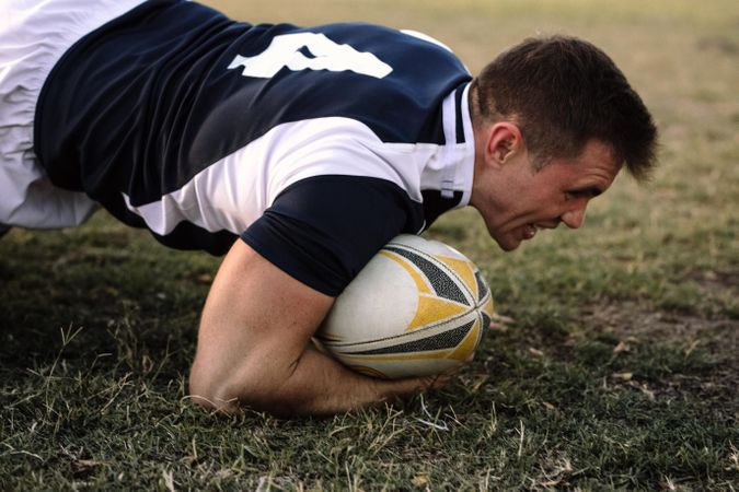 Strong rugby player with ball on ground during the game