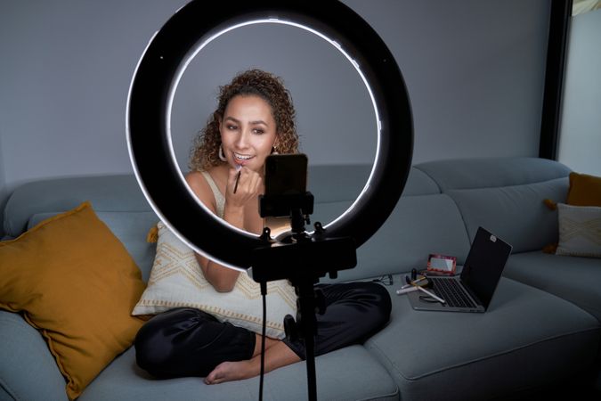 Smiling focused female applying lipstick while recording video o
