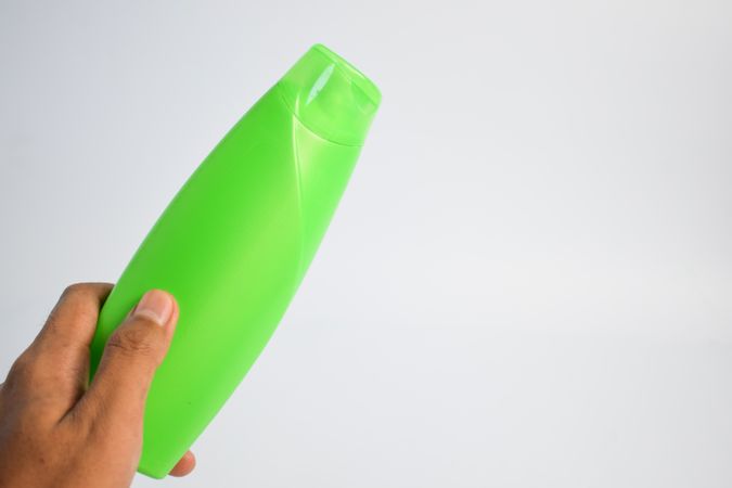 Person's hand holding green shampoo bottle