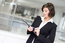 Female in business attire writing on a clip board in a bright office