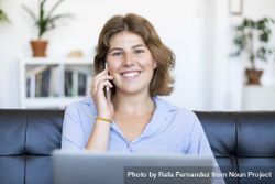 Female entrepreneur sitting on sofa at home using a laptop and chatting on phone 4mWVqz