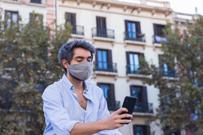 Man in mask browsing smartphone on street