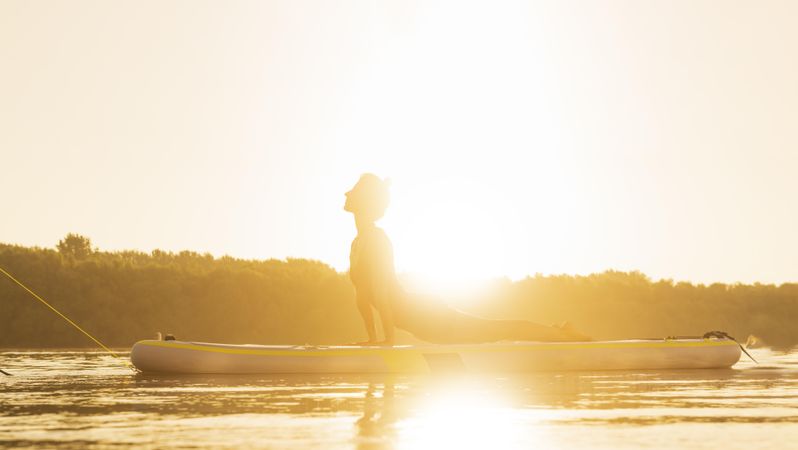 Woman in back stretch on paddleboard on lake in bright sunrise