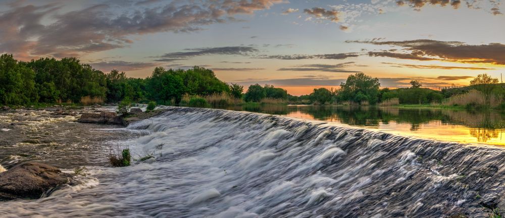 Trees surrounding river under orange sky in Migia, Ukraine