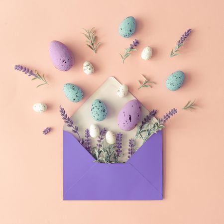 Spring flowers, leaves and Easter eggs on pastel pink background and paper envelope