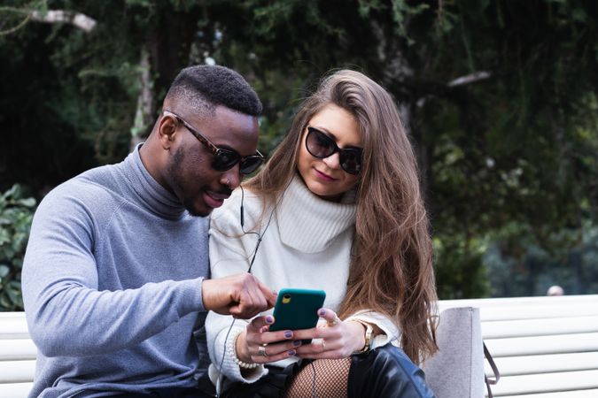 Joyful multiethnic couple listening music on smartphone in park
