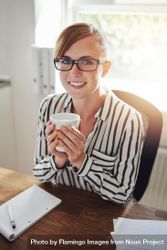 Content female in striped shirt with coffee at her desk 0VkeG5