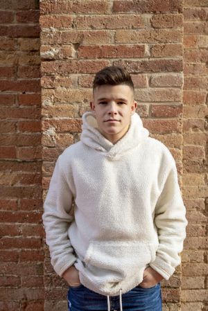 Portrait of serious young male with hands in pocket leaning against brick wall