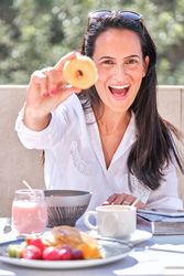 Cheerful woman demonstrating delicious donut while having breakf