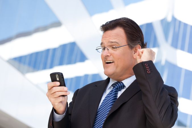 Businessman Looking at Cell Phone Clinches His Fist in Joy