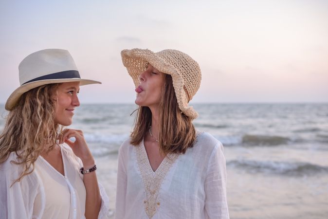 Smiling girlfriends in summer clothes barefoot in water on beach