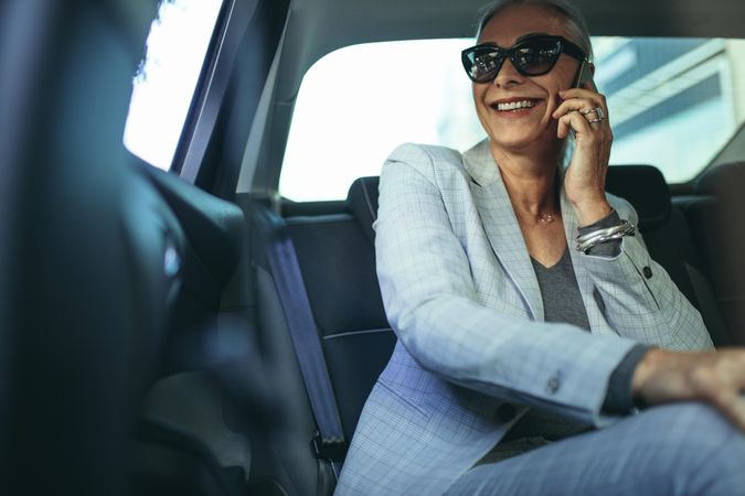 Older businesswoman using phone while traveling by a car