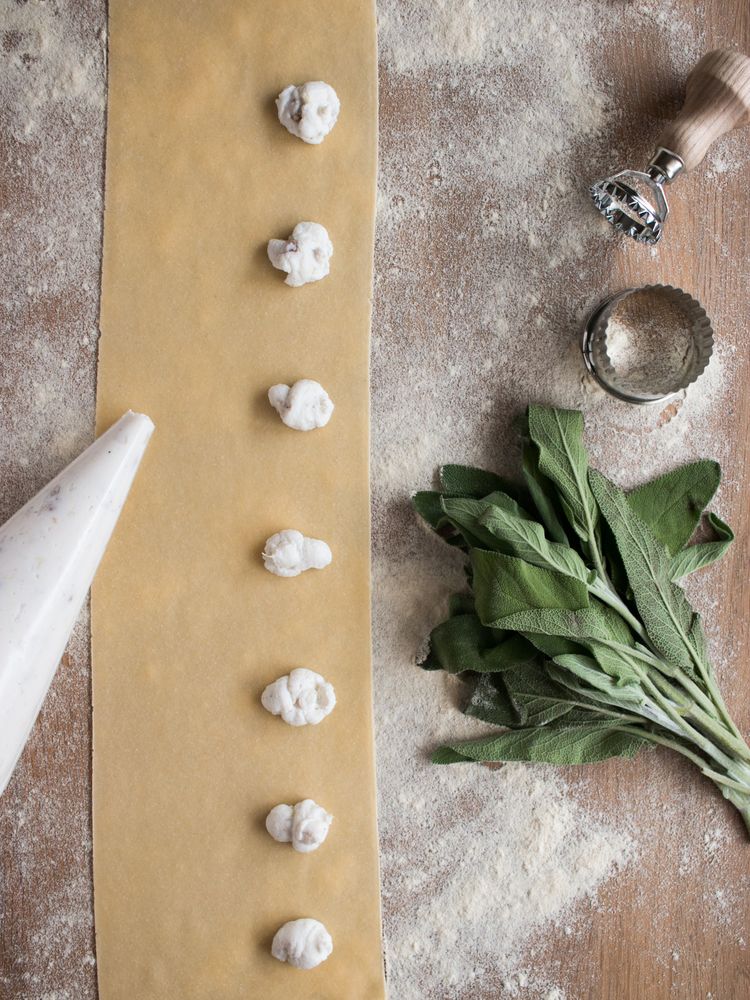 Crop hands squeezing stuffing on ravioli dough near sorrel