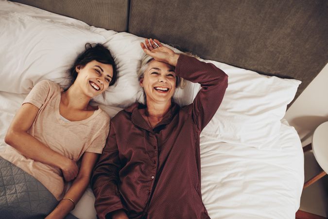 Older mother and adult daughter lying on bed spending time together and laughing