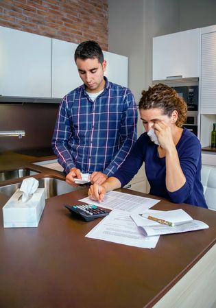 Sad couple going through their bills together in the kitchen with wife crying, vertical