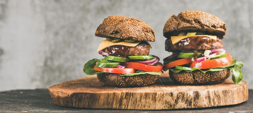 Two cheeseburgers, stacked with fresh vegetables, on wooden board, with copy space