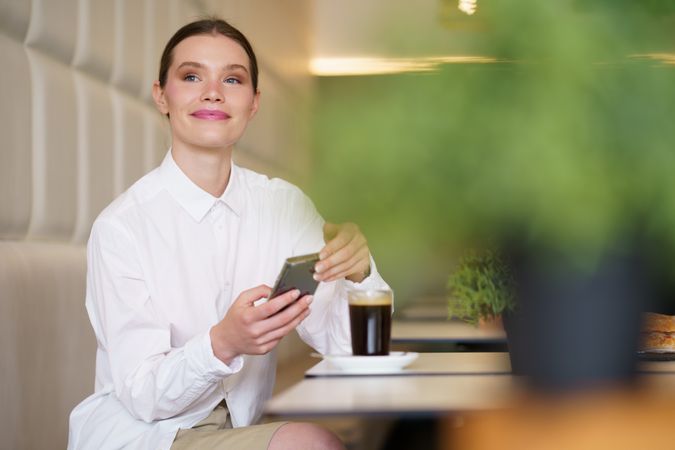 Smiling elegant woman using phone sitting on a cafeteria
