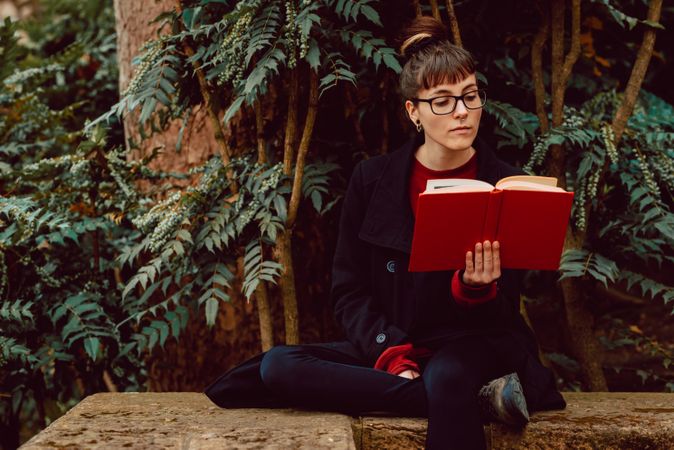 Young woman reading book on bench in park