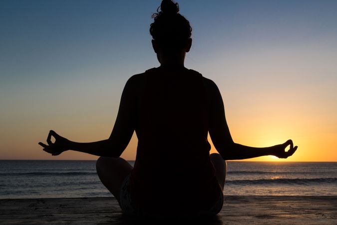 Woman meditating on seashore at sunset