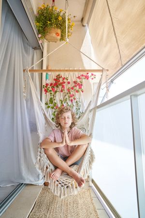 Cute child meditating in hanging chair on balcony