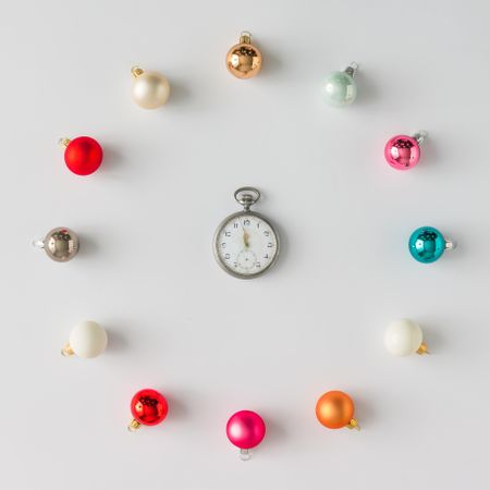 Circular border of colorful Christmas bauble decorations on light background with clock