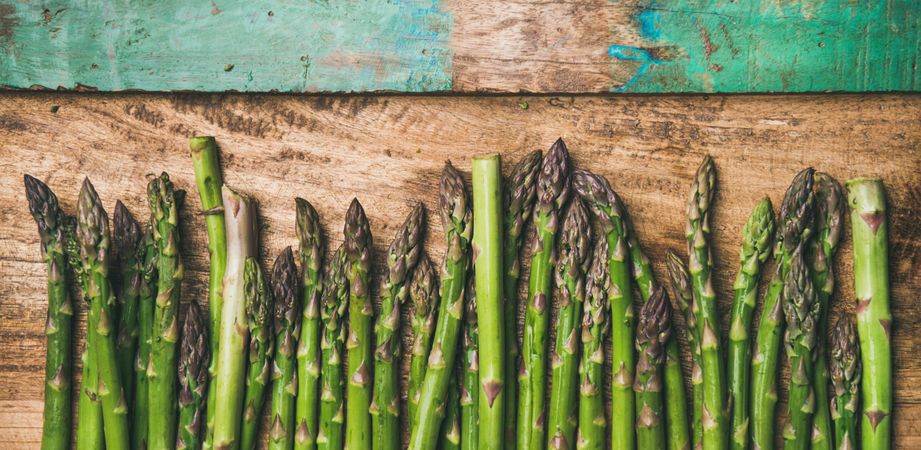 Asparagus lined up on wooden board with green trim, wide composition