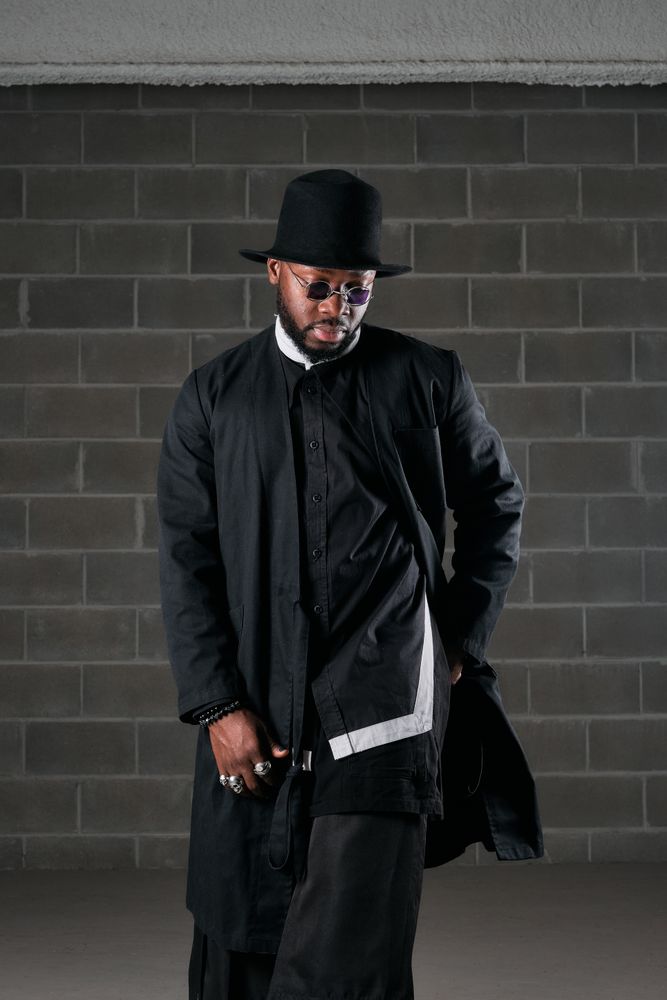 Stylish man in black outfit near brick wall